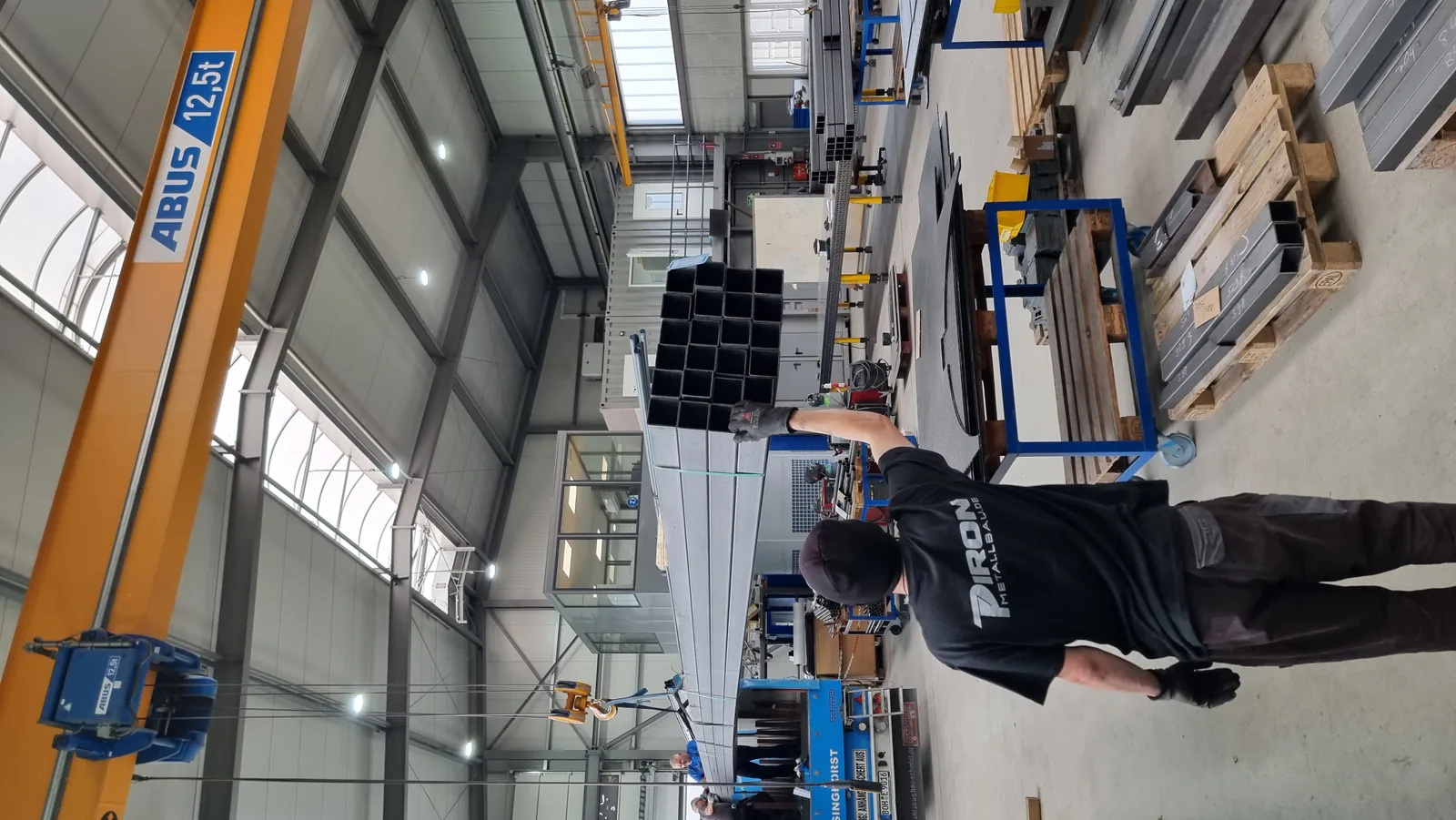 Blick in die Halle mit Hallenkran, ein Mitarbeiter am Stahlrohr des Pylons