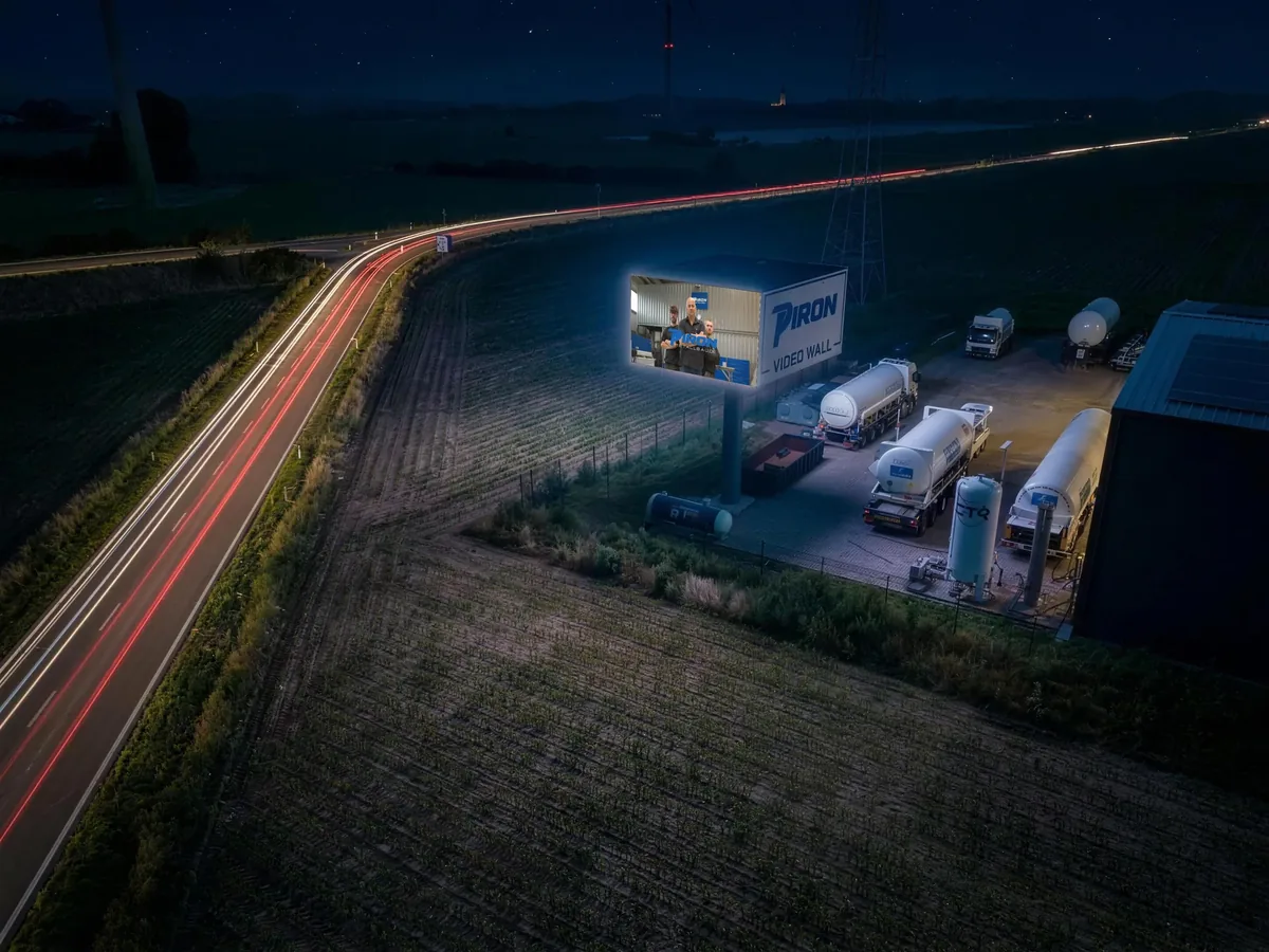Nachtaufnahme aus der Luft: die Wall zeigt PIRON VIDEO WALL, daneben Halle und Fahrzeuge