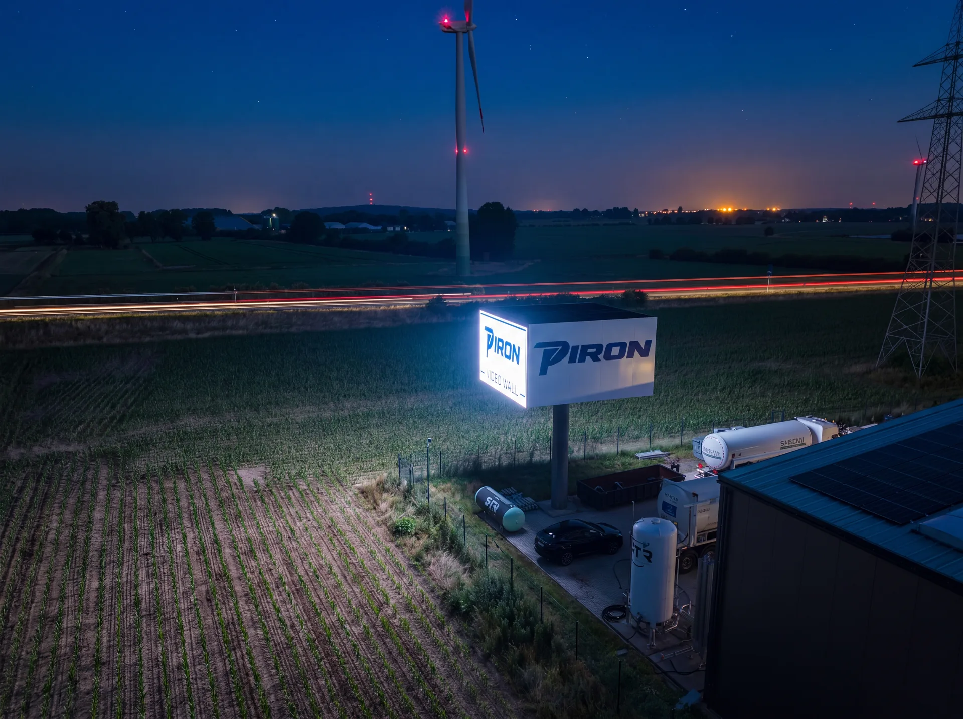 Die Piron LED Wall bei Nacht, leuchtend über dem Gelände, mit den Lichtspuren des Verkehrs auf dem Tweestrom