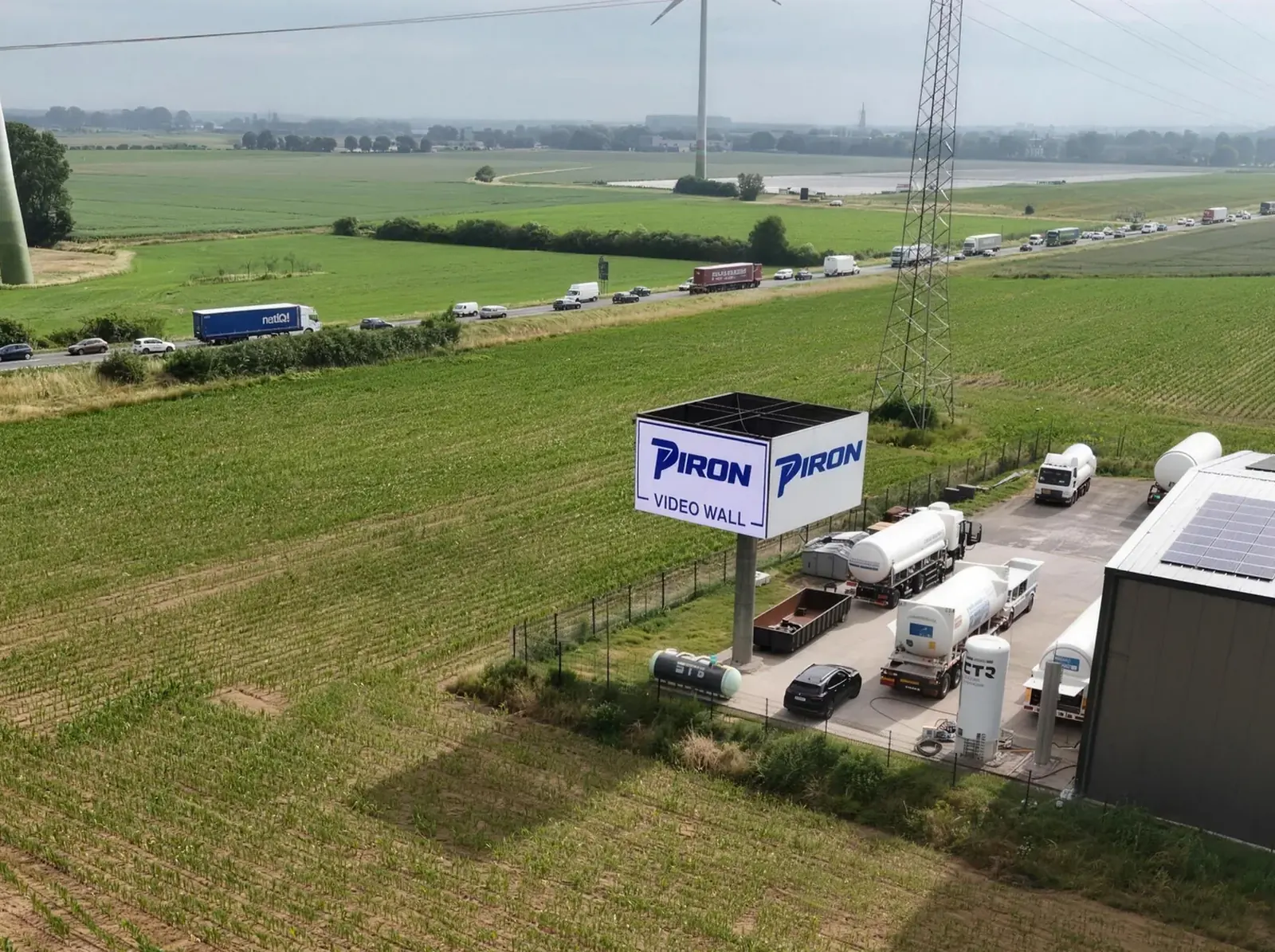 Luftaufnahme bei Tag: die Piron LED Wall am Feldrand neben der Halle, dahinter der Tweestrom mit dichtem Verkehr